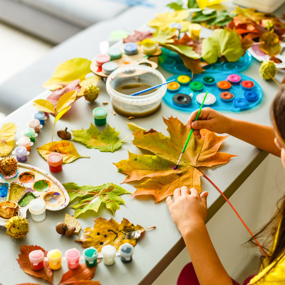 A child using paints to paint a large fall leaf