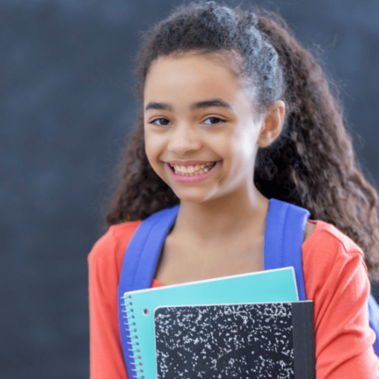 Young girl with a backpack smiling and holding a book