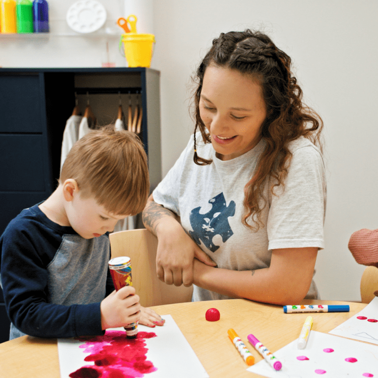 Woman with BlueSprig t-shirt looks at child drawing on a sheet of paper