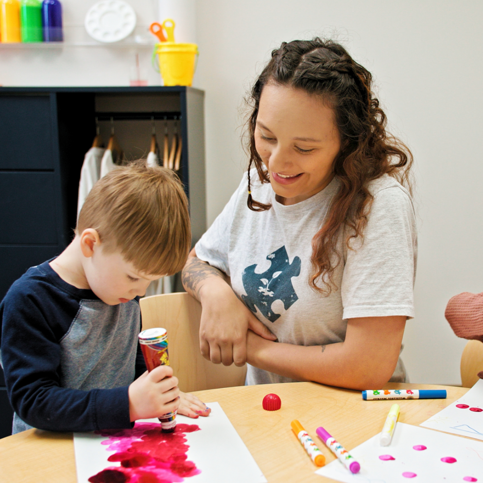 Woman with BlueSprig t-shirt looks at child drawing on a sheet of paper