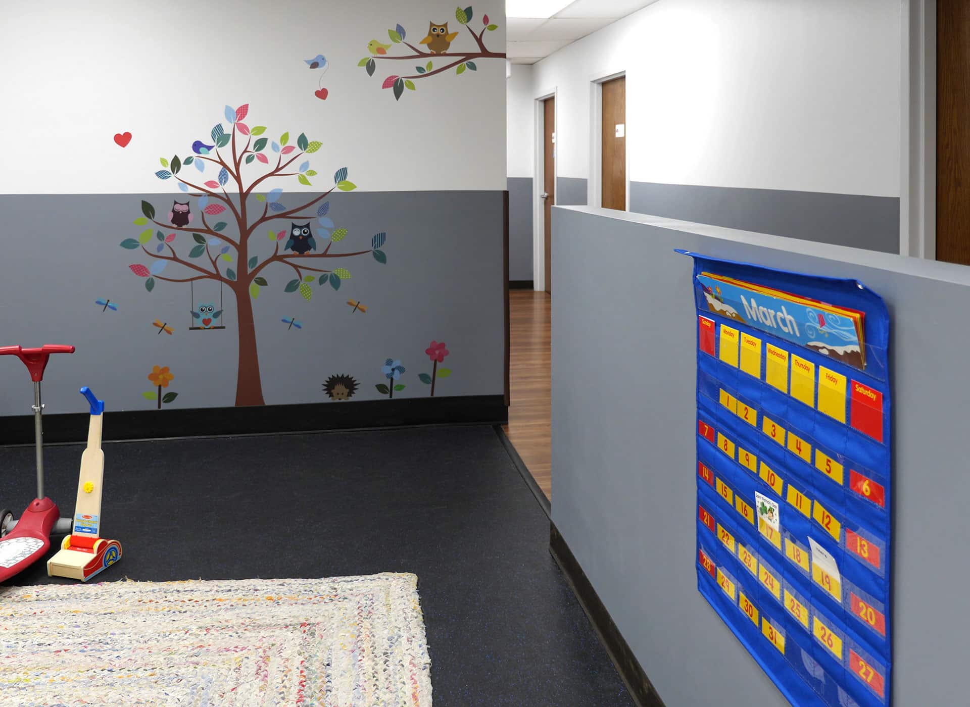 The play area at an autism center with a safety floor and a wall decal shaped like a tree.