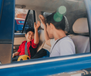 Children high five in the back seat of a car. 