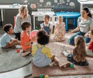Children sit in a circle with two teachers.