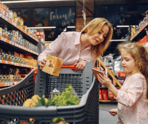 A woman pushes a shopping cart and talks to a young girl.