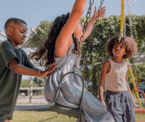 One child pushes another on a swing.